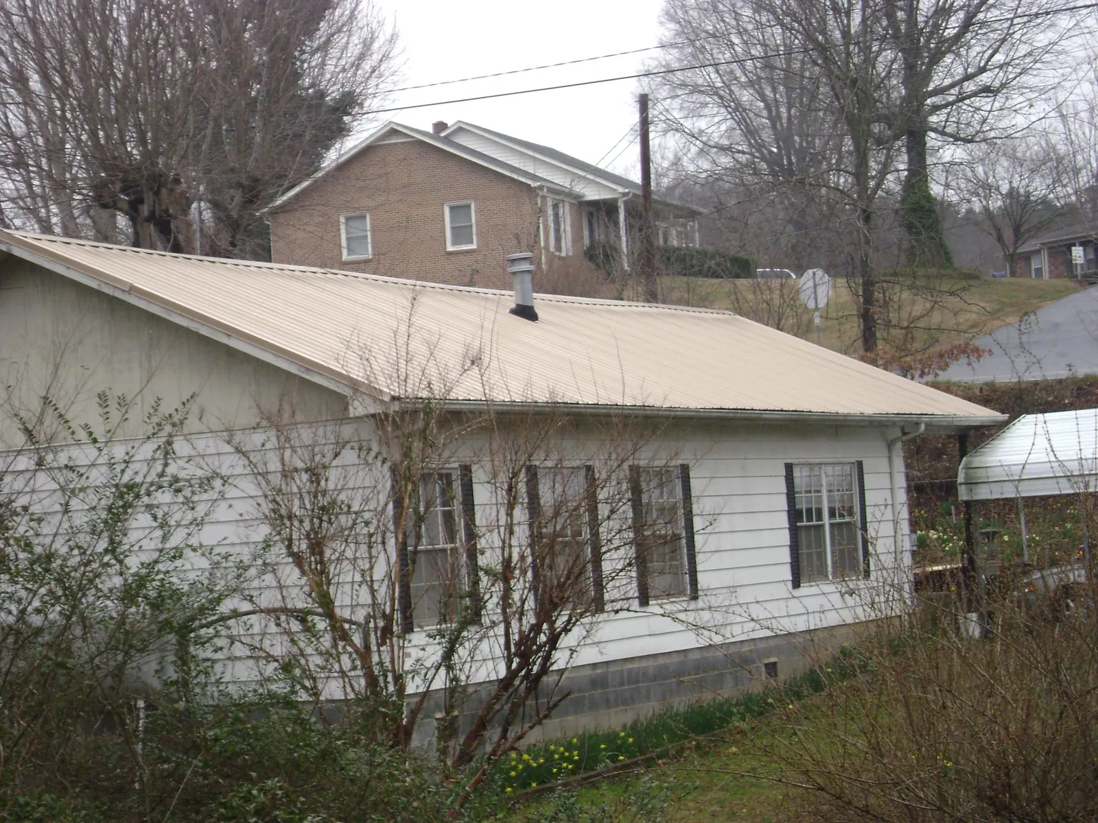 Tan metal roof on a white sided house set into a hillside — Commercial Roofing by Roofing Brothers in Ashland